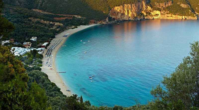 Lichnos beach from above: a long curve of sand below a golden cliff